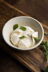 Whole tied Italian cheese burrata on small wooden cutting board served with fresh oregano