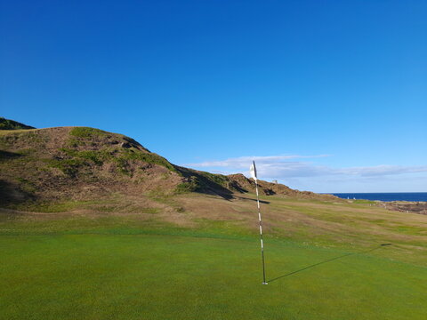 The hardest Par 3 in Britain, The Rockies, on Anstruther golf club in Scotland. The beautiful scenery filled with greenery and under a cloudless sky. The pin the hole with the flag blowing in the wind