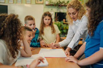 Teacher helping elementary school students with writing exercise in classroom