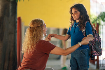 Mother holding hands with daughter at school entrance, back to school