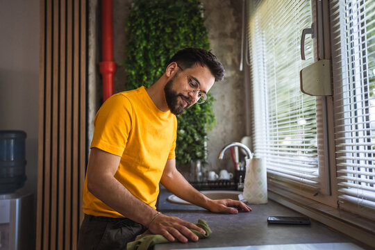 tidy man is wiping and disinfecting a kitchen counter with a rag