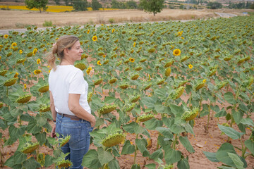 blonde woman wearing jeans and a white t-shirt walking through a field of sunflowers