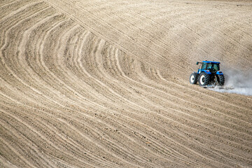 A tractor moves across freshly plowed wavy soil, highlighting agricultural machinery and rural productivity in a minimalist landscape.