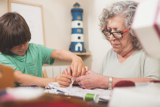 Child learns to sew guided by his grandmother during a quiet family moment