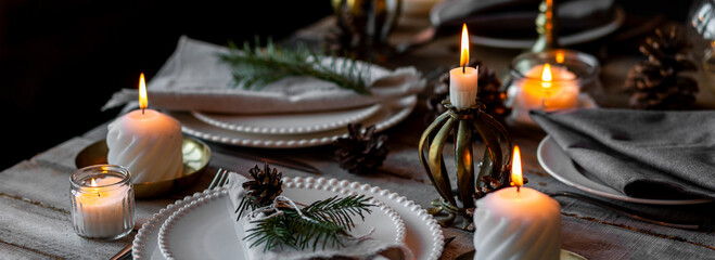 Rustic elegant table decor for Christmas family dinner. Center piece with white candle, pine cone, fir tree branches. Zero waste eco-friendly home decoration. Cozy atmosphere, wooden background banner