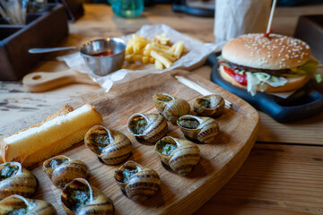 Delicious escargot with fries and burger on wooden table in bistro setting