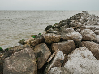 Rock jetty extending into calm ocean waters under overcast sky, natural coastal barrier with moss-covered stones and gentle waves, serene seascape landscape for nature and travel themes