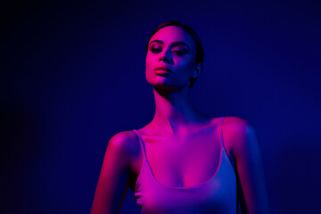 Young woman illuminated by vibrant pink and blue neon lighting against a dark background, exuding...