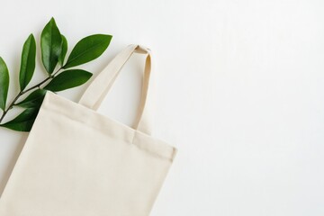 Aesthetic composition of a beige tote bag with green leaves on a clean white background surface top view