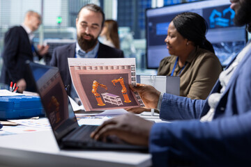 Industrial plant managers look over schematics, planning facility upgrades using laptop. Factory...