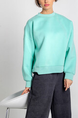 Portrait beautiful woman of model appearance. Girl in mint jumper, black trousers on grey background. Pretty female with trendy makeup posing in studio. Vertical photo.