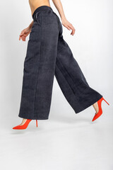 Portrait beautiful woman of model appearance. Girl in black trousers, red shoes on grey background. Vertical photo.