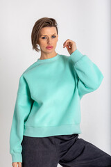 Portrait beautiful woman of model appearance. Girl in mint jumper, black trousers on grey background. Pretty female with trendy makeup posing in studio. Vertical photo.