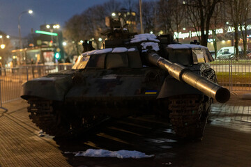 Military tank displayed at night in a city square with snow, representing historical significance and current events