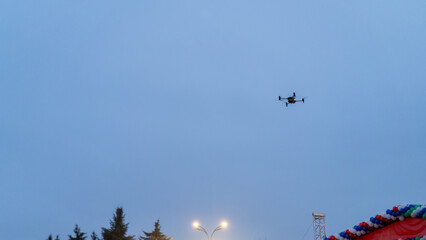 Drone flying over festival area during overcast evening with colorful decorations in the background