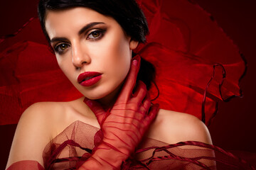 Elegant portrait of a glamorous young brunette woman with vibrant red makeup and fashionable attire