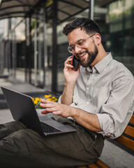 Adult man tourist sit on bench use laptop and talk on cellphone