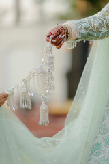 Bride holds a silver kalira, a traditional Indian wedding ornament, against her light green dress,...