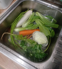 Top view Clean and soak vegetables,  coriander, carrots, Chinese kale, green beans, and cabbage in the sink on wooden background, protect, clean, fresh, copy space