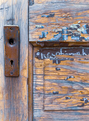 Old wooden door with lock used as a sign or menu board has old paint with letters and is worn without finish in spots. This is a vintage panel wood door.