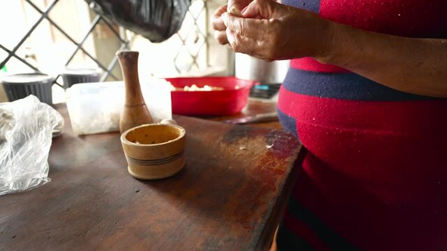 Skilled female cook peeling fresh garlic cloves using wooden mortar, working in rustic kitchen with traditional culinary techniques