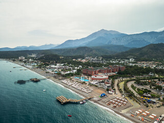 Fototapeta premium Aerial view of Kemer beach with turquoise Mediterranean sea, crystal clear water and Taurus mountains in the background, Antalya, Turkey 