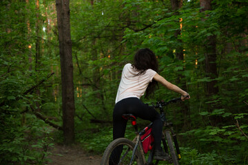 Beauty smiling sport woman biking on bicycle on path among green trees in a forest summer...