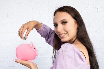 A Young Woman Engaging in the Activity of Saving Coins in a Charming Pink Piggy Bank