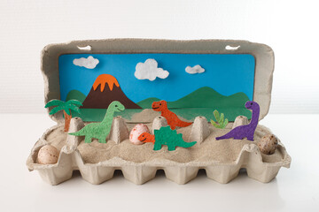 Prehistoric dinosaur world diorama with volcano and eggs inside egg carton, ideal for kids education, school crafts, homeschooling kits, science museums, book illustrations, toy packaging, © Elena