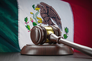 Wooden Gavel Resting on Table In Front of Mexican Flag.