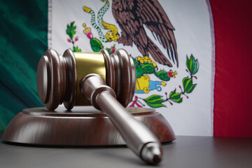 Wooden Gavel Resting on Table In Front of Mexican Flag.