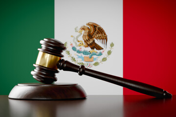 Wooden Gavel Resting on Table In Front of Mexican Flag.