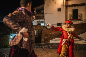 Spanish men in traditional colonial clothing dueling with swords called foils and daggers in a...