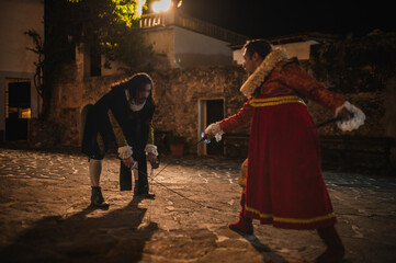 Spanish men in traditional colonial clothing dueling with swords called foils and daggers in a...