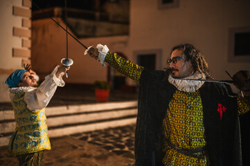 Spanish men in traditional colonial clothing dueling with swords called foils and daggers in a traditional 1600s town setting.