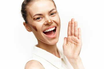 Cheerful young woman with diverse skin tones smiling and waving, wearing a white shirt, expressing joy and positivity against a light background.