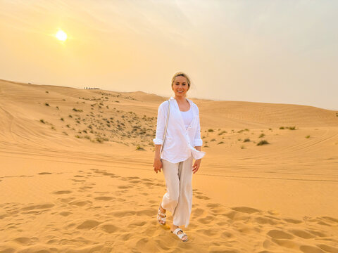 Portrait of a beautiful woman walking on sand dunes in the desert at sunset, looking at camera, smiling.