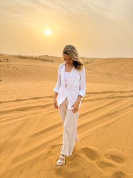 Portrait of a beautiful woman walking on sand dunes in the desert at sunset.