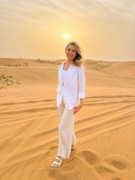 Portrait of a beautiful woman walking on sand dunes in the desert at sunset, looking at camera, smiling.
