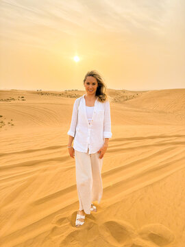 Portrait of a beautiful woman walking on sand dunes in the desert at sunset, looking at camera, smiling.