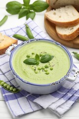 Tasty pea cream soup with basil served on white wooden table