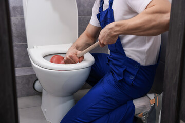 Plumber unclogging toilet with hand plunger indoors, closeup