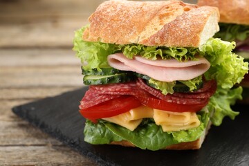 Tasty baguette sandwich with ham and vegetables on wooden table, closeup