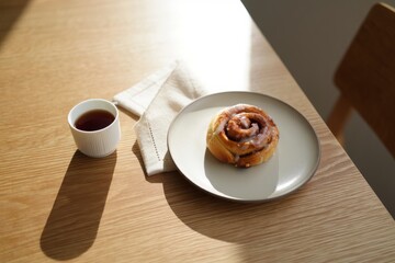 Fresh cinnamon roll on a plate with cup of black coffee in morning sunlight