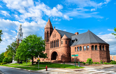 The historic Billings Library, built in red sandstone with Romanesque Revival architecture, stands beside the white clock tower of Ira Allen Chapel on the University of Vermont campus in Burlington