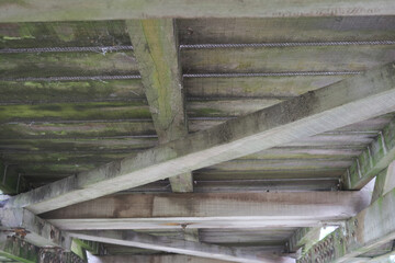 The wooden beams of a bridge are covered in moss and dirt