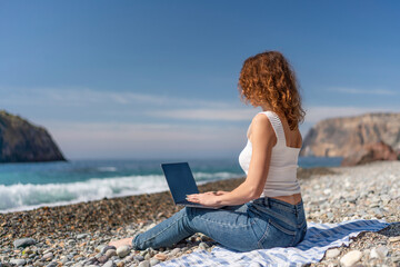 Beach Laptop Woman works remotely on sunny day, pebble beach location for vacation.