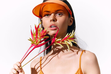 Vibrant model wearing a sporty visor and holding tropical flowers, expressing summer joy with a bright, warm color palette and stylish fashion statement.