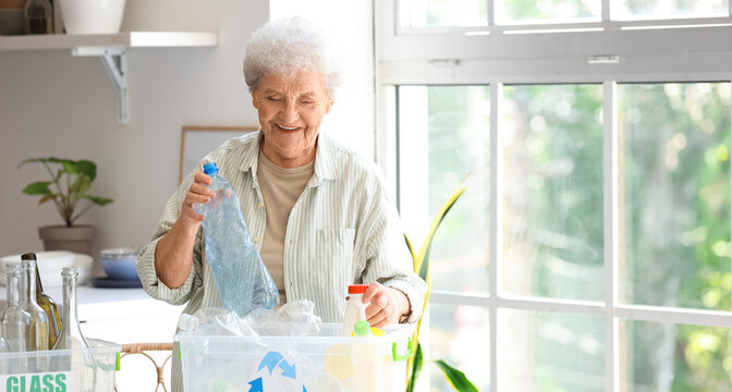 Senior woman with container of garbage on table in kitchen. Waste sorting concept - Powered by Adobe