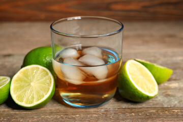 Glass of rum with ice and lime on wooden table